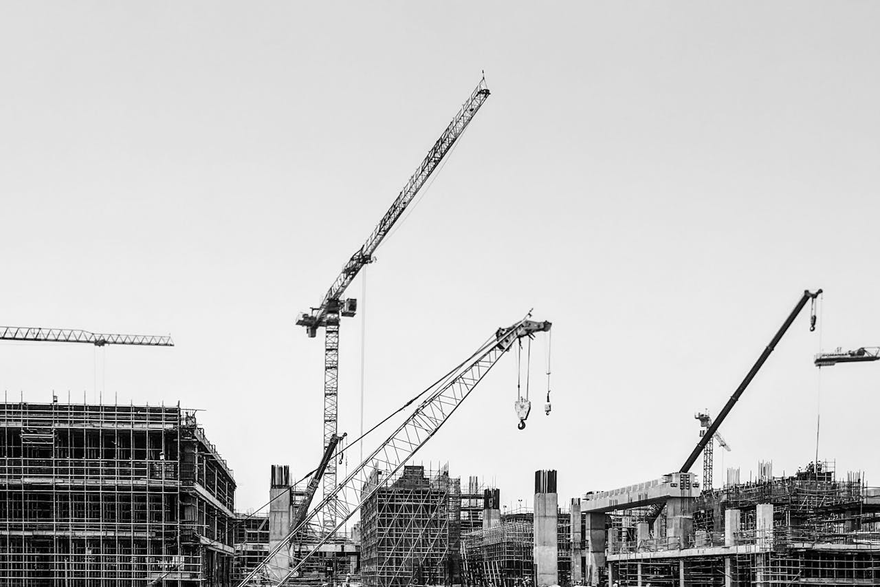 Black and white image of cranes working on a large construction site under a clear sky.