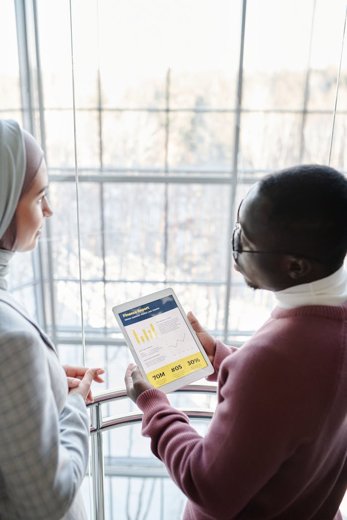 Two professionals discuss data displayed on a tablet by a window.