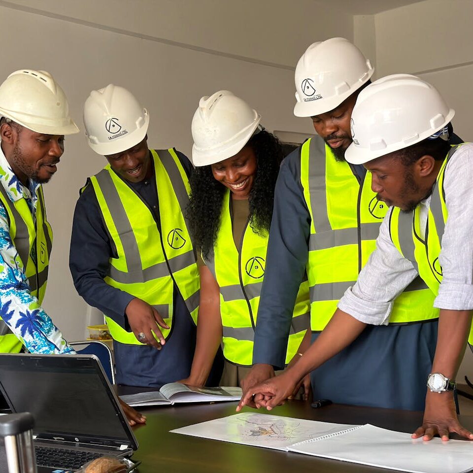 pexels photo 37198881 Group of engineers in hard hats and safety vests reviewing blueprints in an office setting.